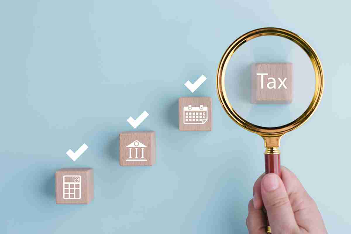 © Bussarin / stock.adobe.com Lupe vergrößert Holzklotz mit Aufschrift Tax